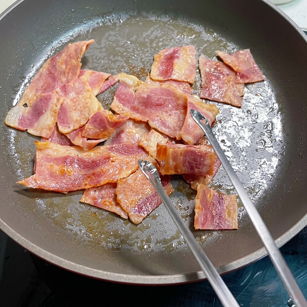 カリカリのベーコンと一緒に、卵をフライパンで調理している様子。