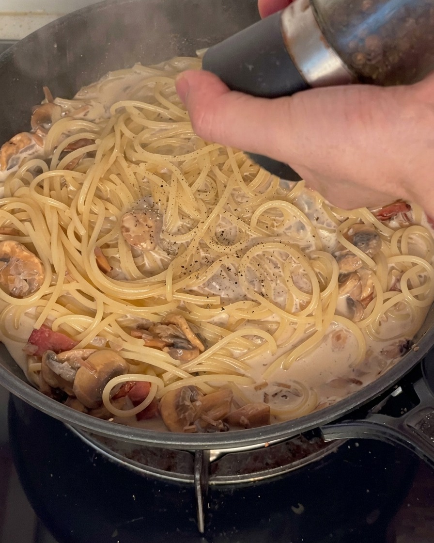 クリームソースのパスタに、黒胡椒を挽きかけている様子。