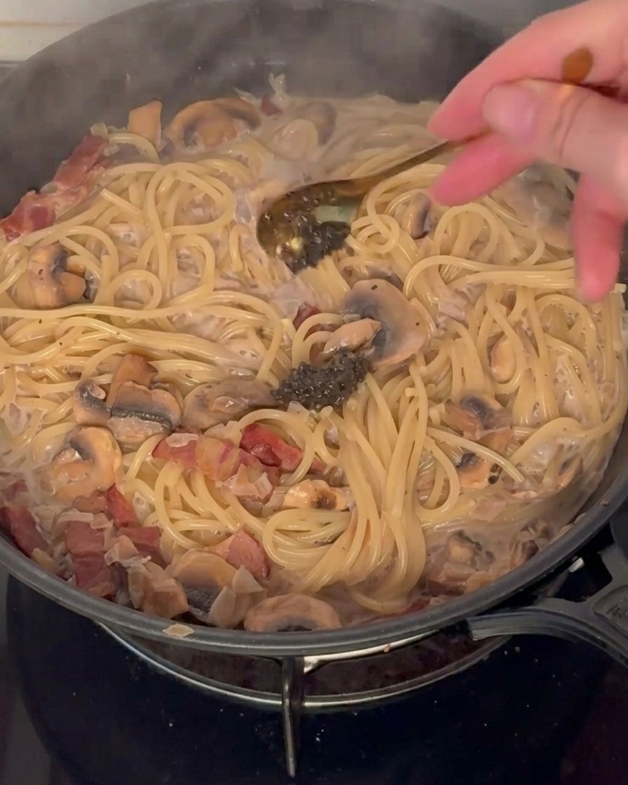 クリームパスタに黒トリュフペーストをスプーンで加えている様子。