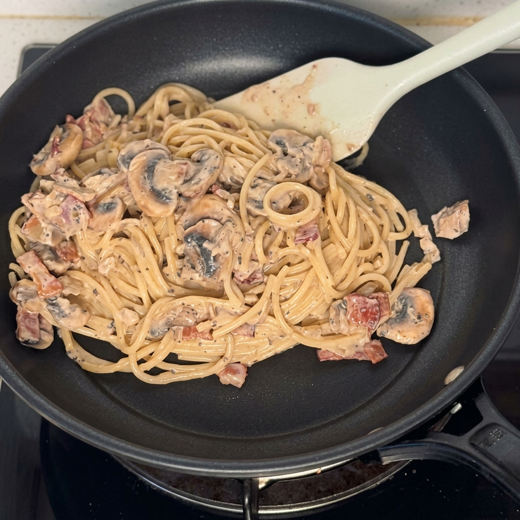 ソースが絡まったスパゲッティ、きのこ、ベーコンが入ったフライパン。