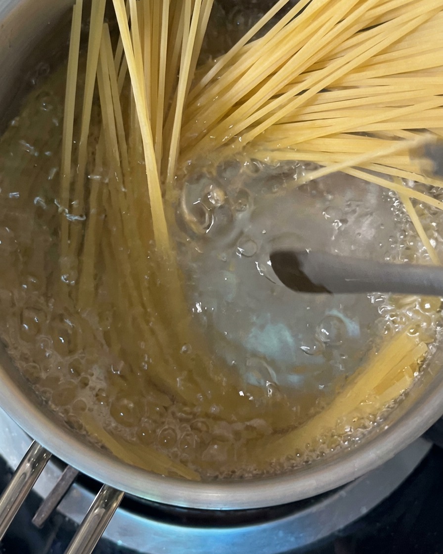 ステンレス製の鍋の中で沸騰したお湯に押し込まれる乾燥スパゲッティ。