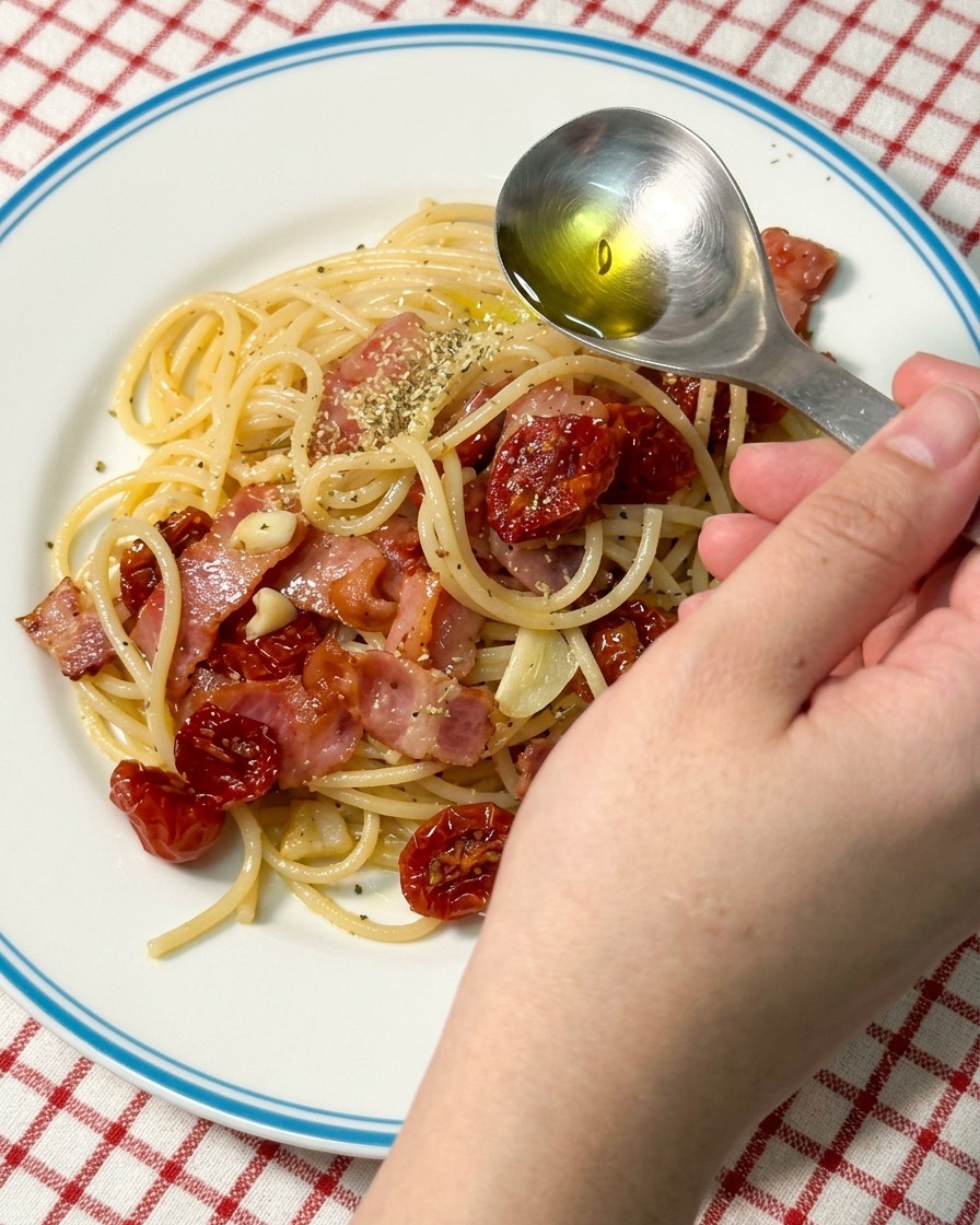 盛り付けられたパスタの上から、スプーンを使って黄金色のオリーブオイルを回しかけているアップの画像。