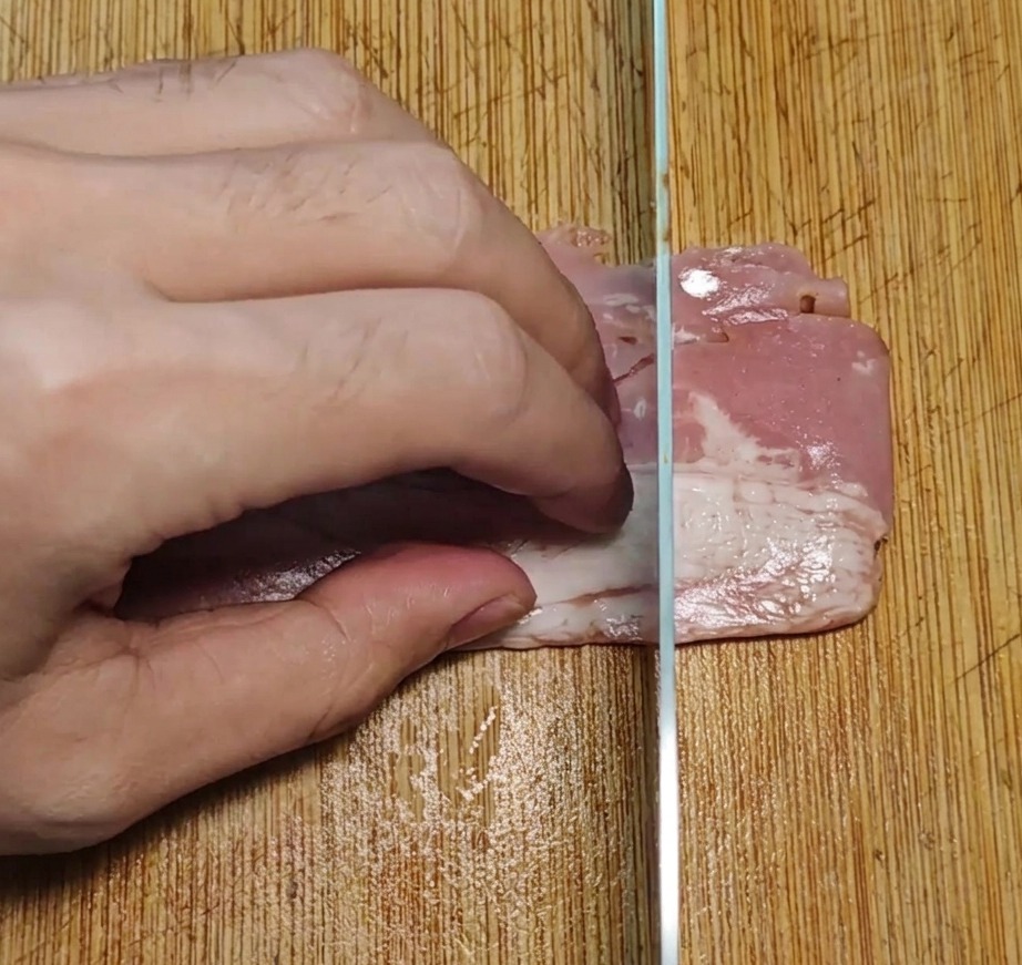 まな板の上でベーコンを包丁で均一な長方形に切っている様子。