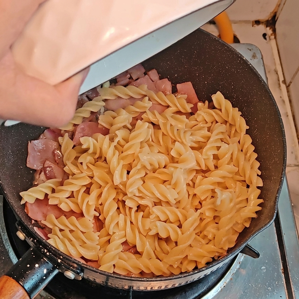 フライパンに茹でたパスタとアスパラガスを投入している様子。