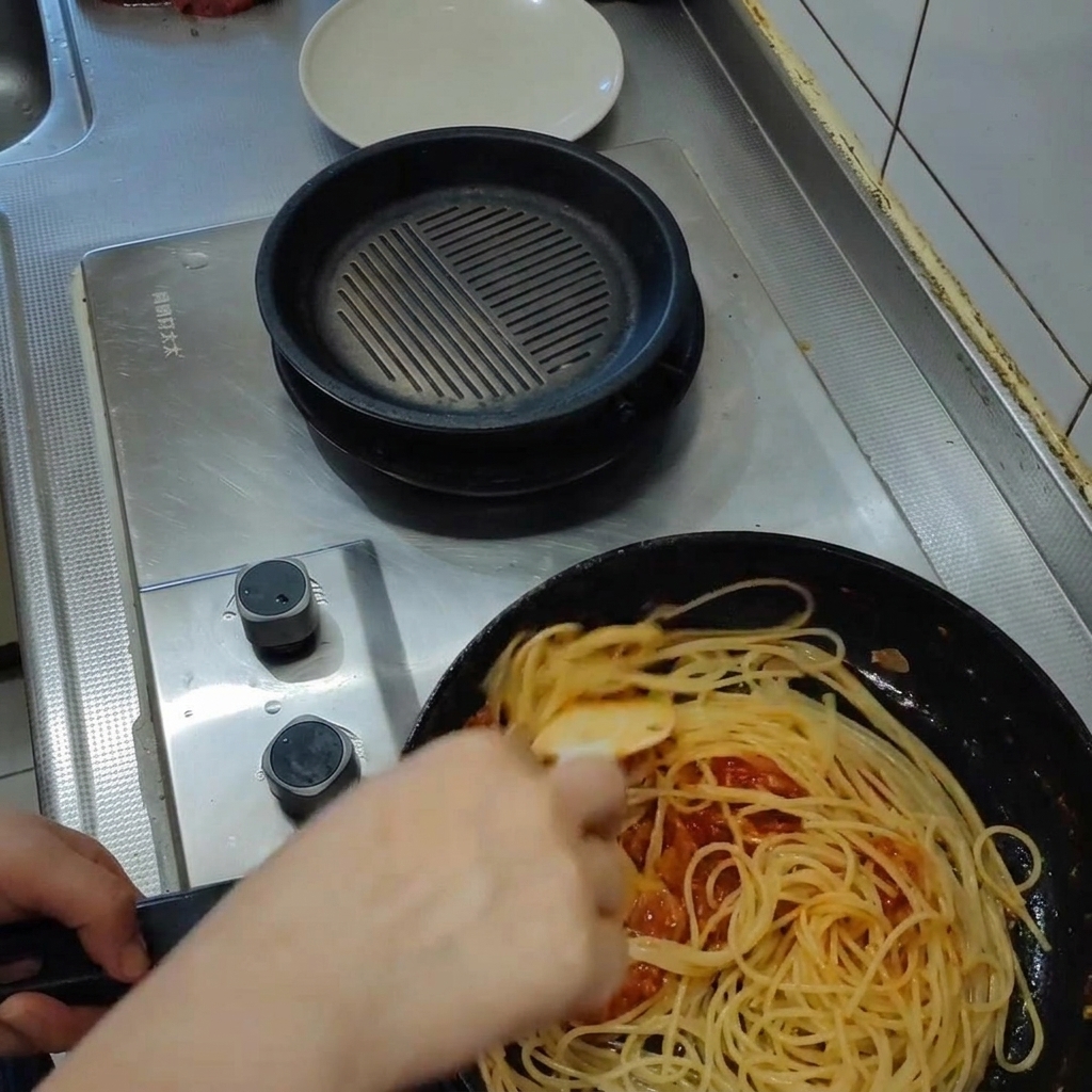 フライパンの中でパスタとソースを絡めている様子。蒸気が上がり、ソースがとろりと乳化している。