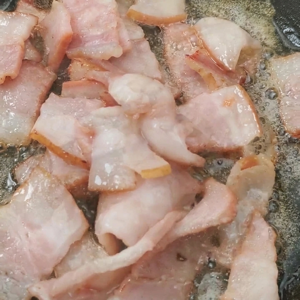 カリカリのベーコンと一緒にフライパンでトマトが炒められている様子。