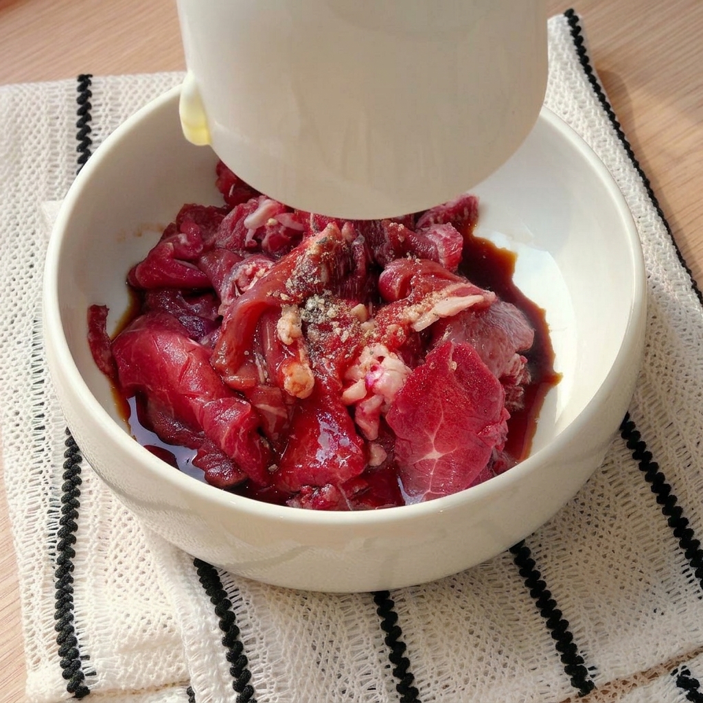ボウルに入った生の牛肉に、調味料を加えて下味をつけている様子。