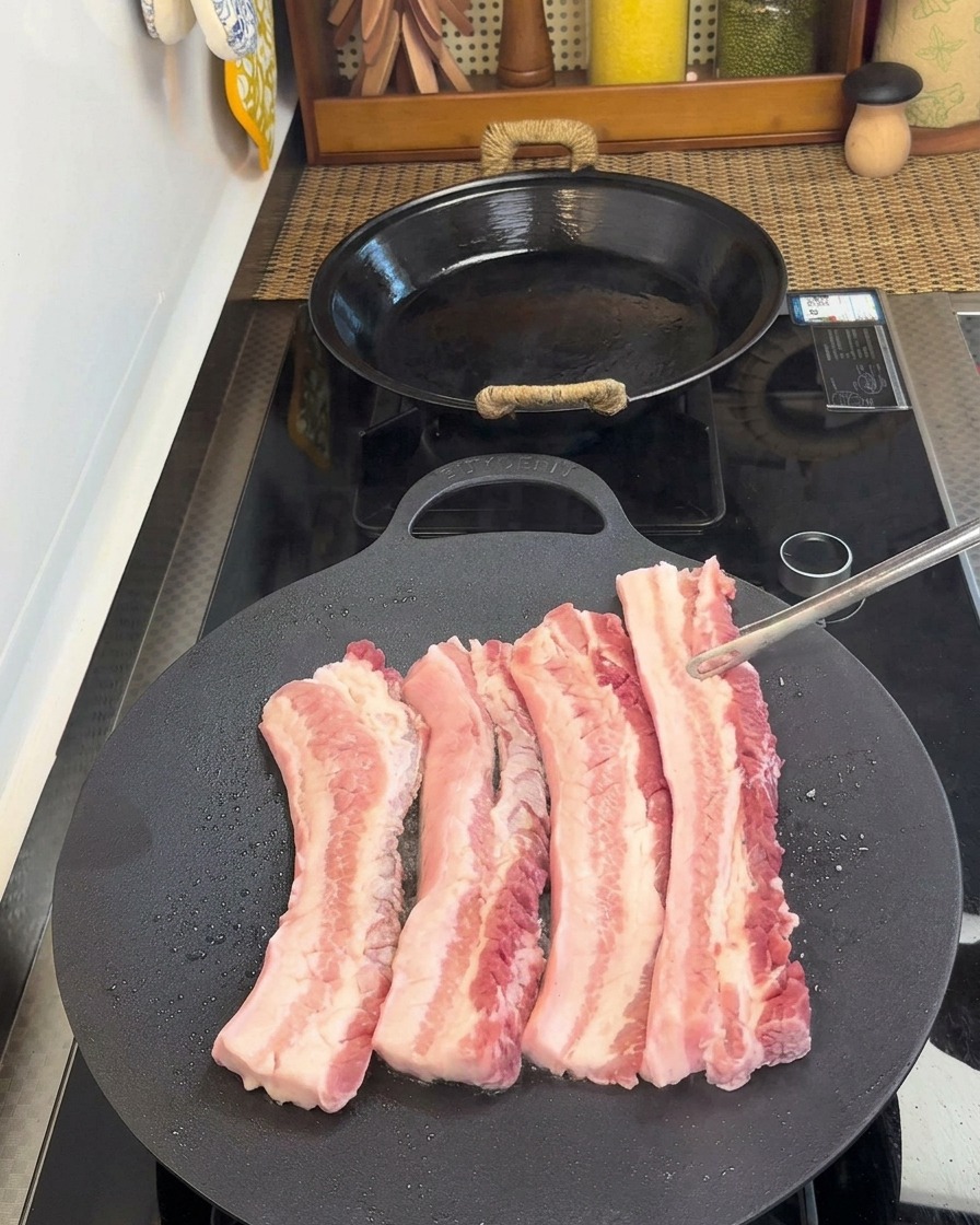 トングで豚バラ肉を裏返し、焼けた面を見せている様子。