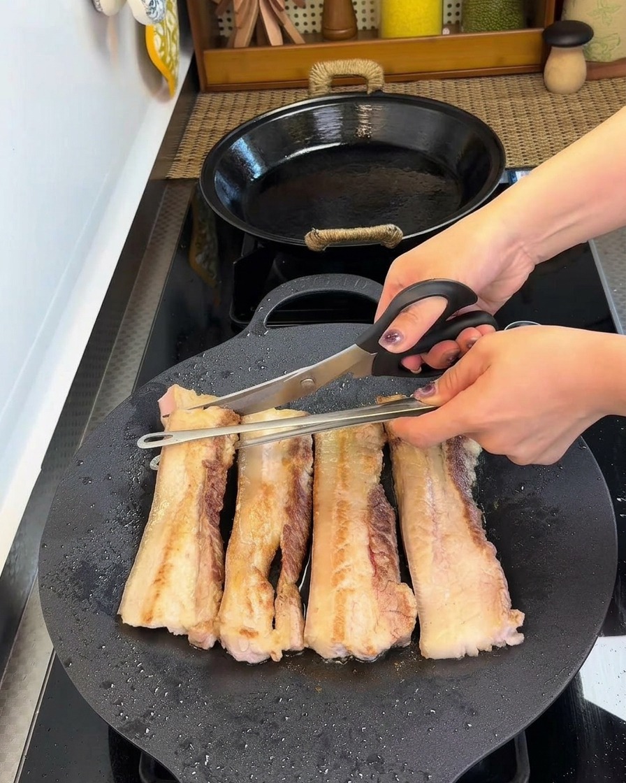 キッチンバサミでフライパンの中の豚バラ肉をカットしている様子。