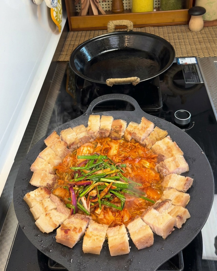 焼いている豚肉とキムチの上に、刻んだ野菜と調味料をかけて仕上げる様子。