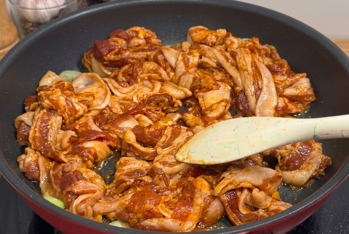 焼き上がった豚バラ肉を、フライパンの中でキッチンバサミを使って一口サイズに切っている様子。