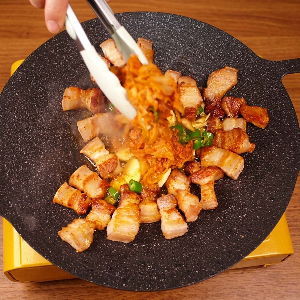 トングを使って、焼けた豚バラ肉とキムチを全体的に混ぜ合わせている様子。