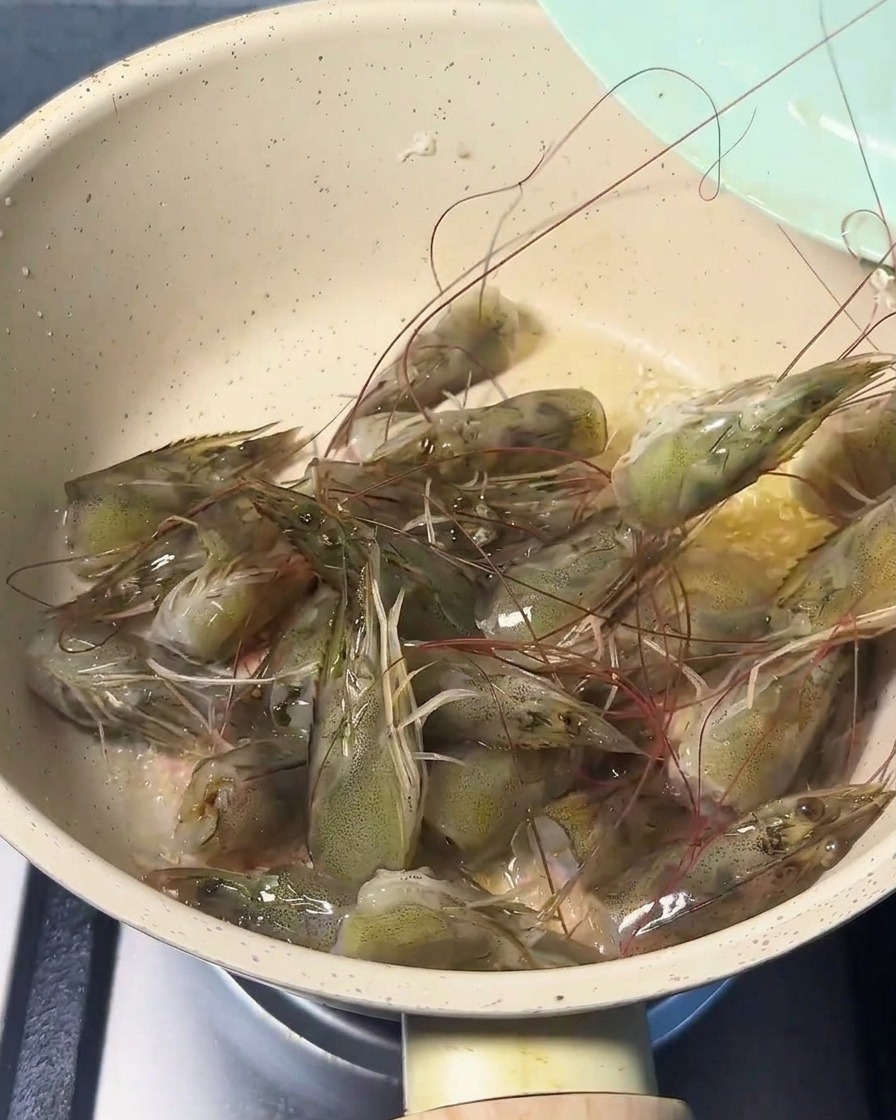 フライパンで海老の頭を炒めている様子。ピンク色に色づいている。