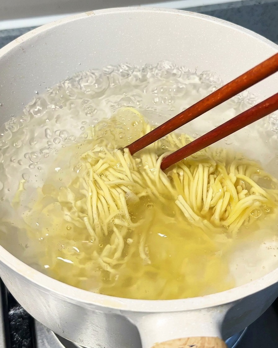大きめの鍋で麺を茹で、菜箸でかき混ぜている様子。