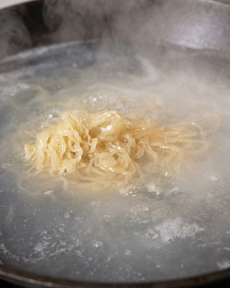 茹で上がった麺を沸騰したお湯から菜箸で引き上げている様子
