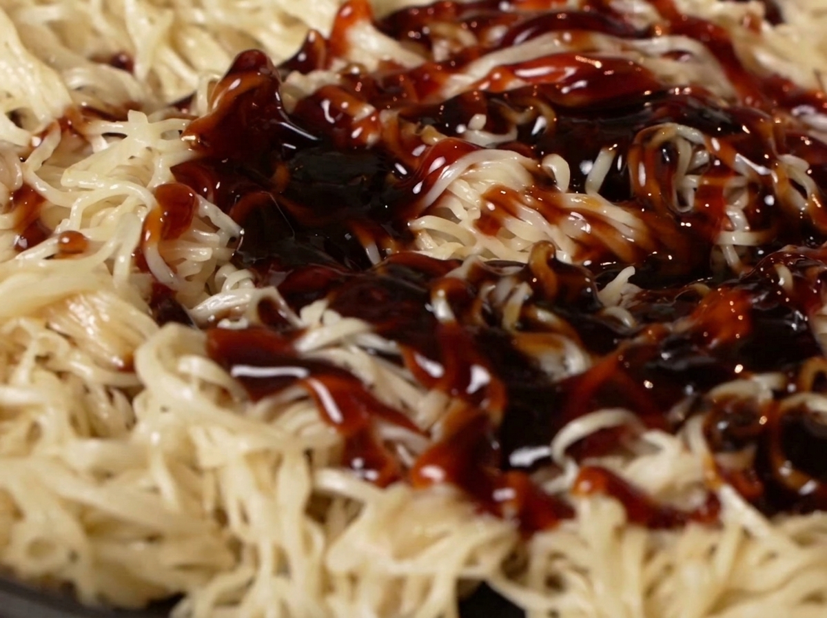 フライパンの中の麺にオイスターソースと醤油をかけている様子