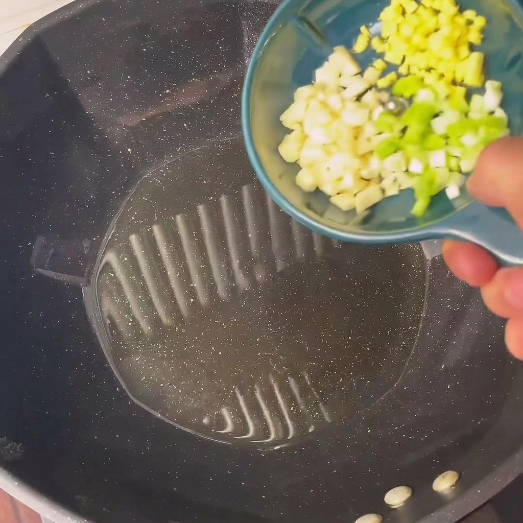 刻んだ青ねぎとにんにくを中華鍋で炒めている様子。