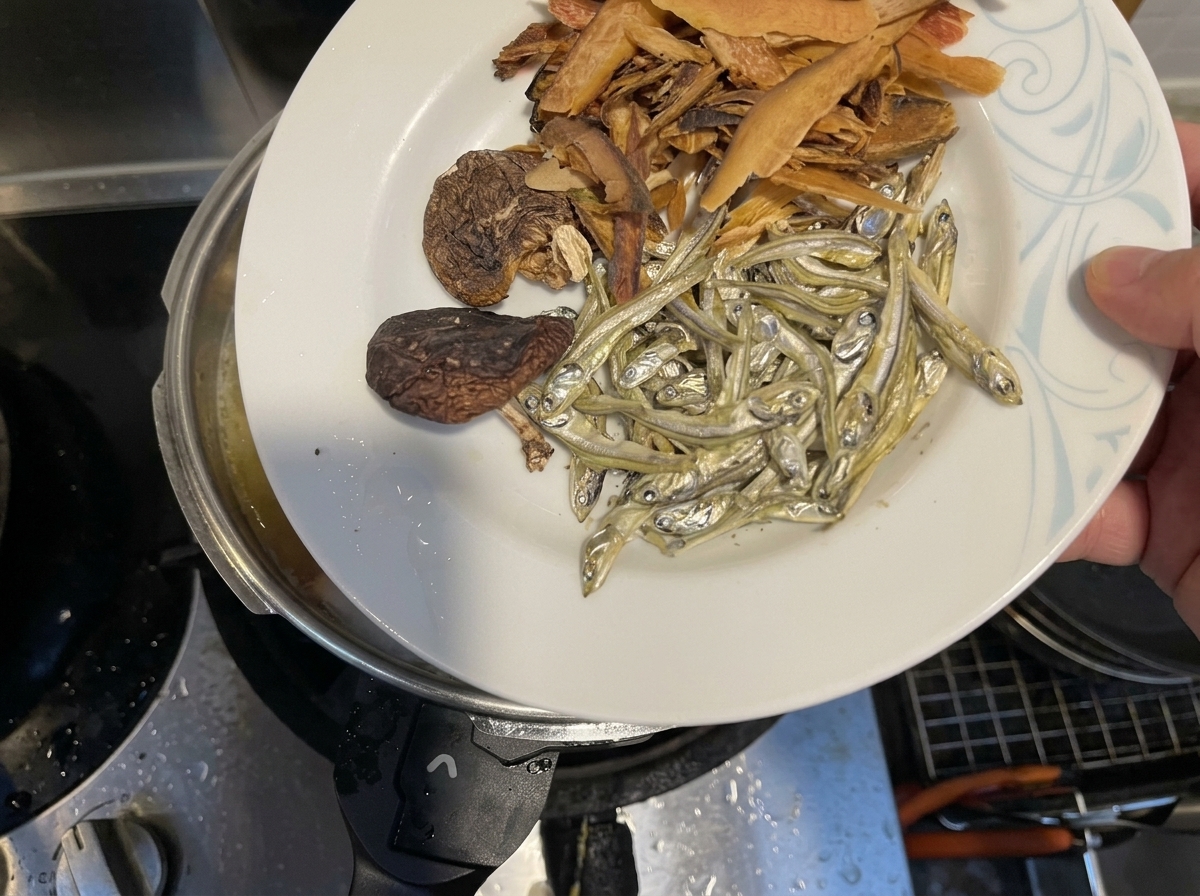 鍋の中に残りの煮干し、干し椎茸、かつお節を投入している様子。