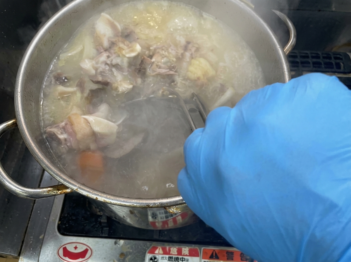 大きな鍋の中でスープを勢いよくかき混ぜ、白濁させる様子。