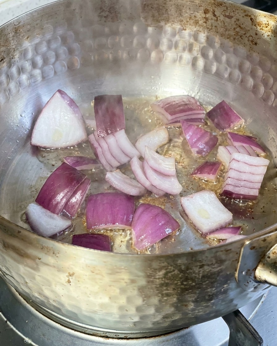 フライパンでスライスした赤玉ねぎが熱せられた油で炒められている様子。