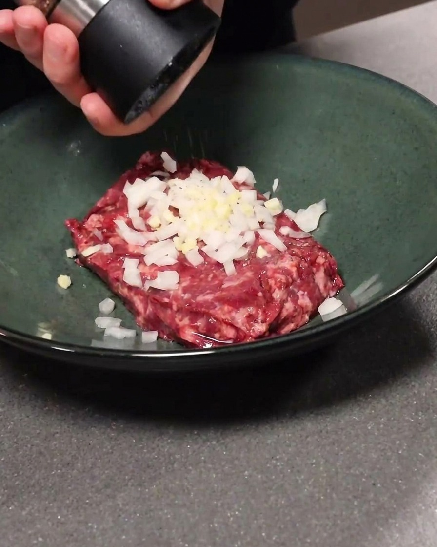 ボウルに入ったひき肉、にんにく、玉ねぎに黒こしょうを加える様子。
