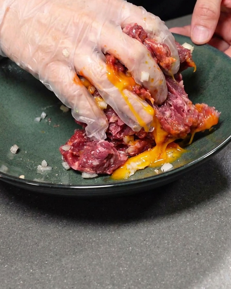 下味をつけたひき肉に卵黄を加えて混ぜ合わせる様子。