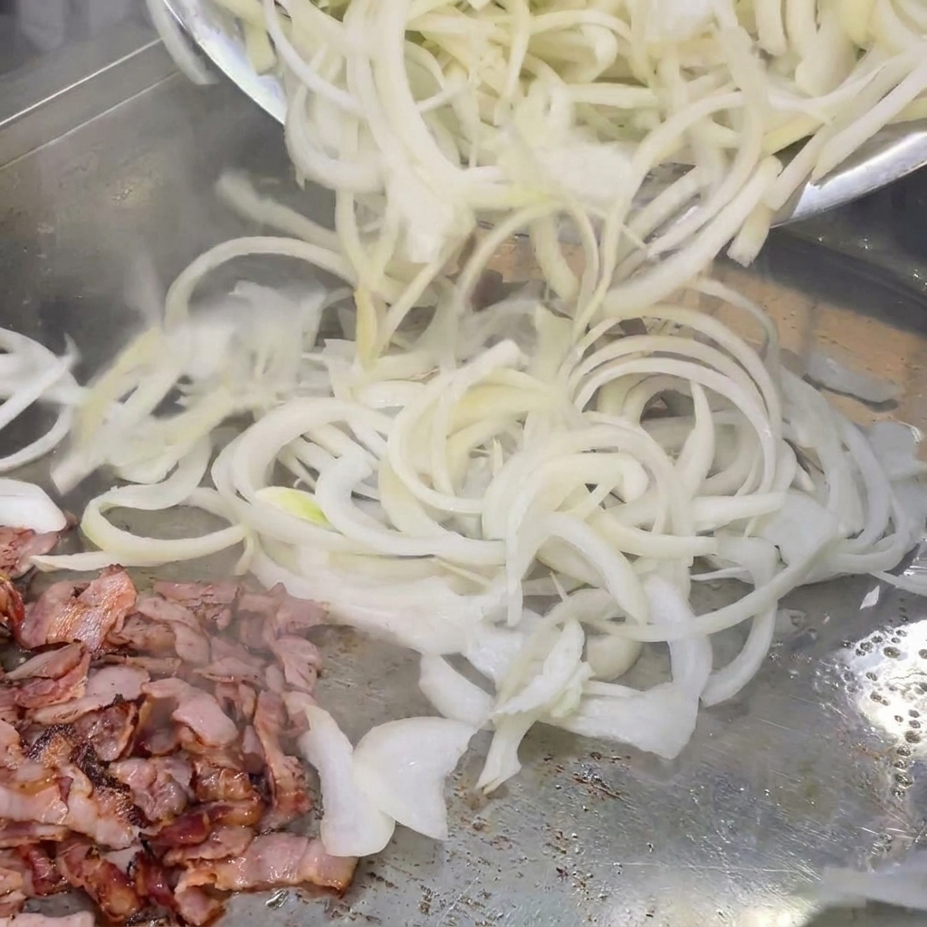 焼いたベーコンの上で一緒に混ぜ合わせられるスライス玉ねぎ。