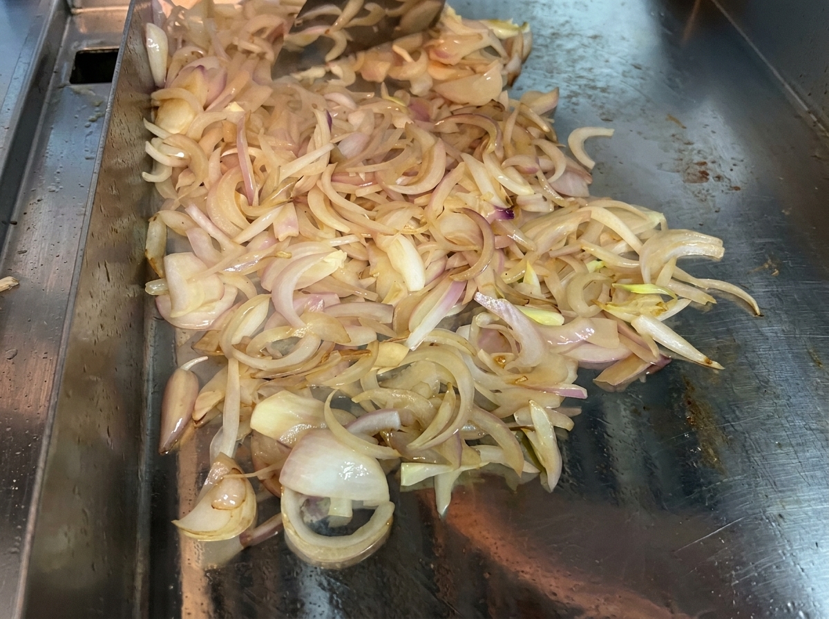 平らな調理面で、玉ねぎをスパチュラで絶えず混ぜながら柔らかくキャラメル状に炒めている様子。