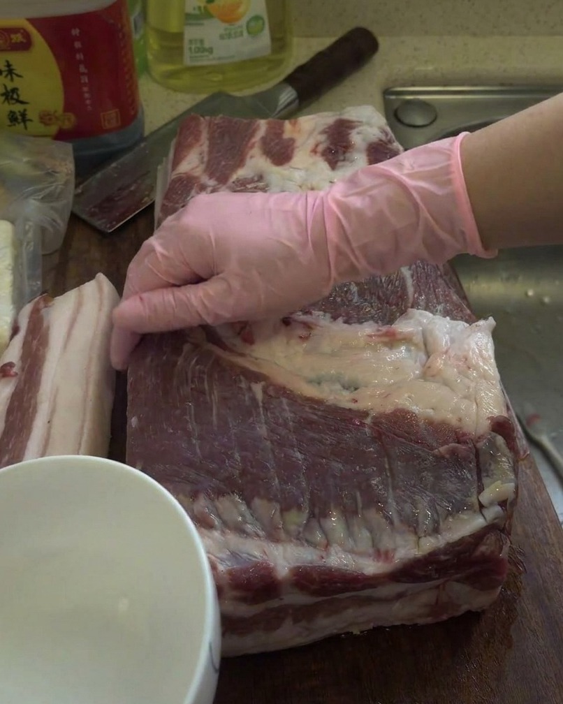木のまな板の上で、生の豚バラ肉の塊に白酒を塗り込んでいる様子。