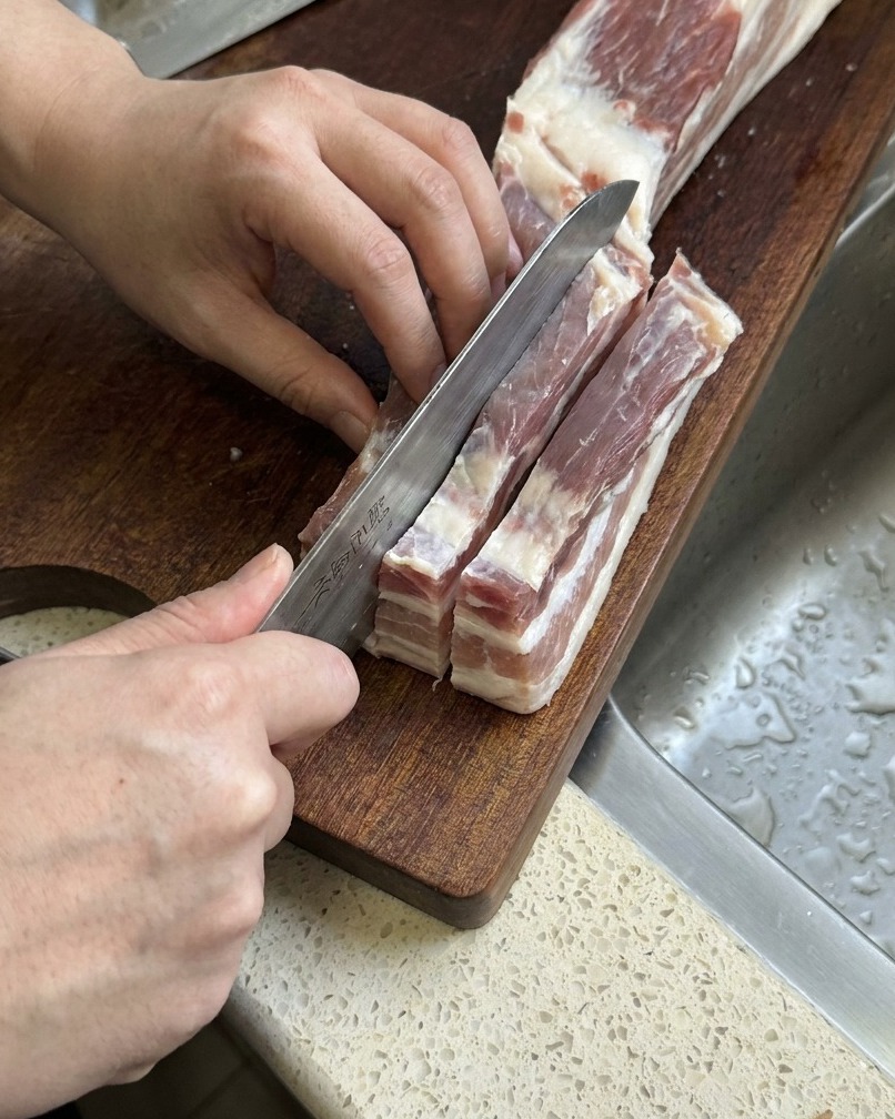 生の豚バラ肉を包丁で厚みのある細長いストリップ状に切っている様子。