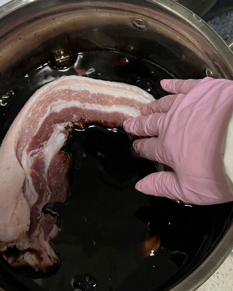 細長く切った豚バラ肉が、濃い醤油色のタレの中に浸かっている様子。