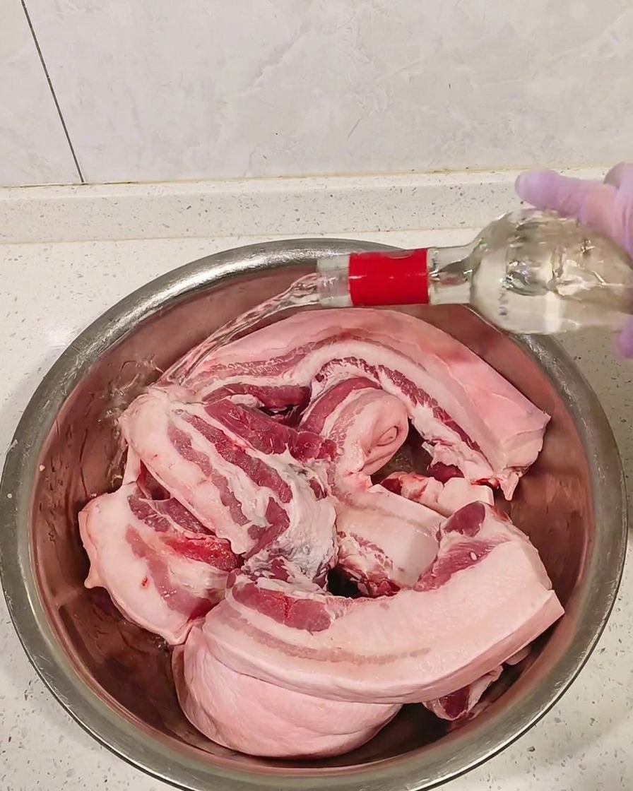 ボウルに入った豚バラ肉に白酒をかけている様子