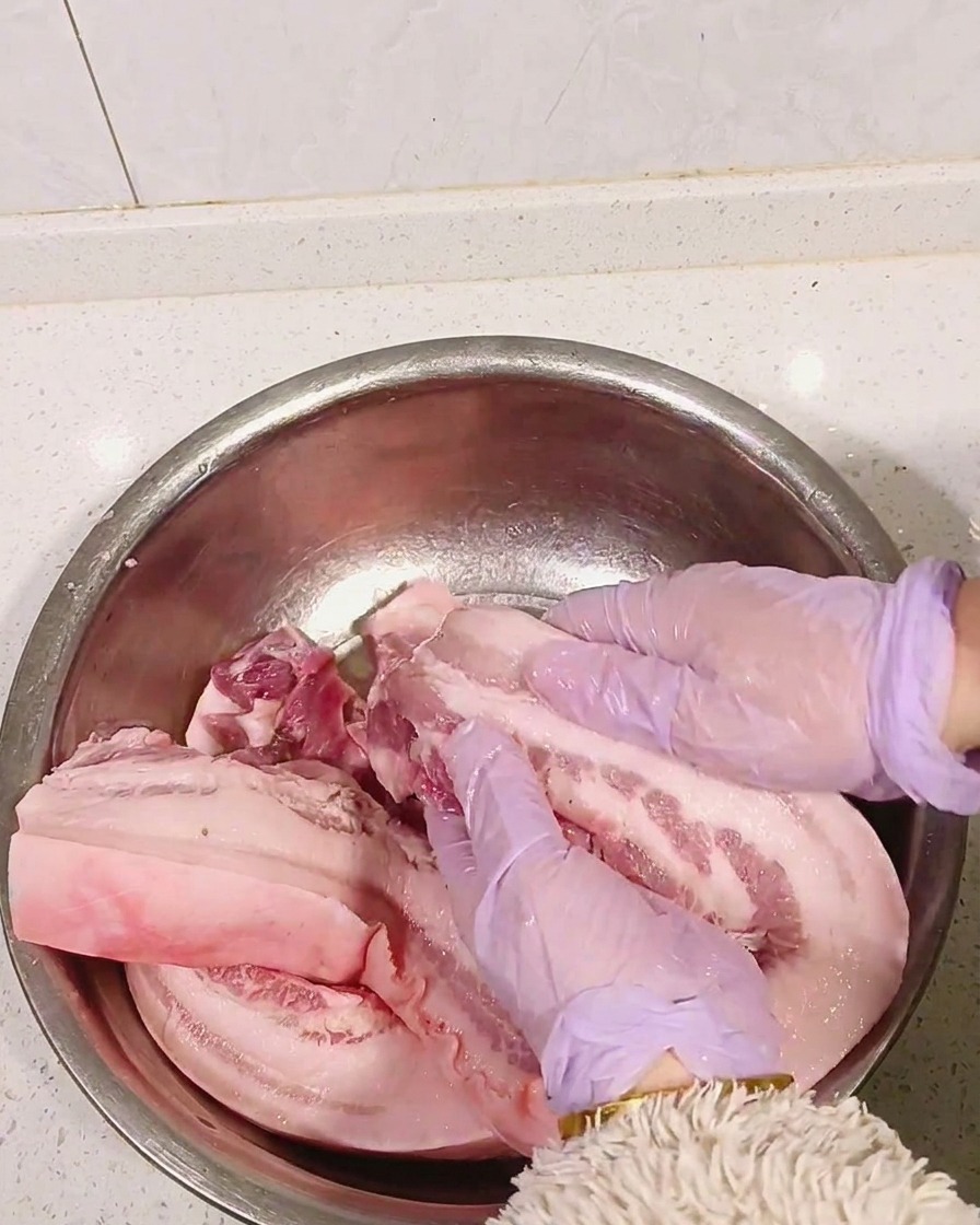 手袋をした手で豚バラ肉に白酒を揉み込んでいる様子
