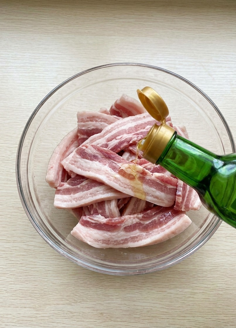 ボウルに入った豚バラ肉に、瓶から醤油を注いでいる様子。