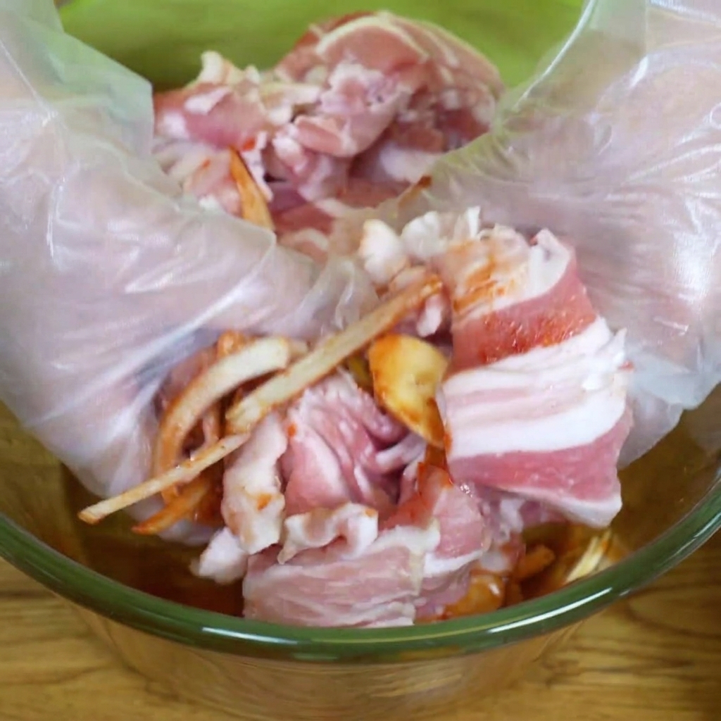 ビニール手袋をして、ボウルの中で肉とタレを混ぜ合わせている様子。