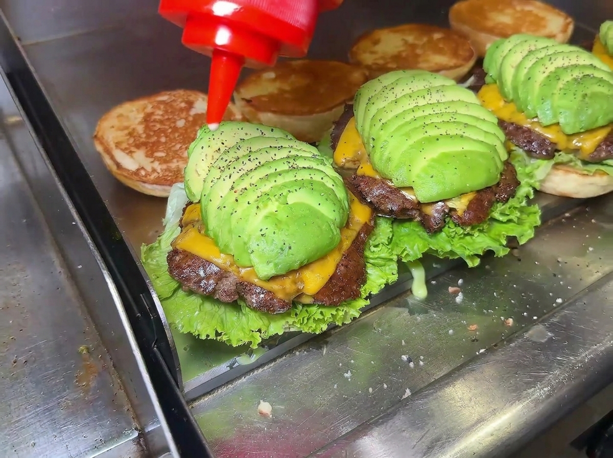 組み立てられたアボカドチーズバーガーに、ソースがかけられているクローズアップ画像。
