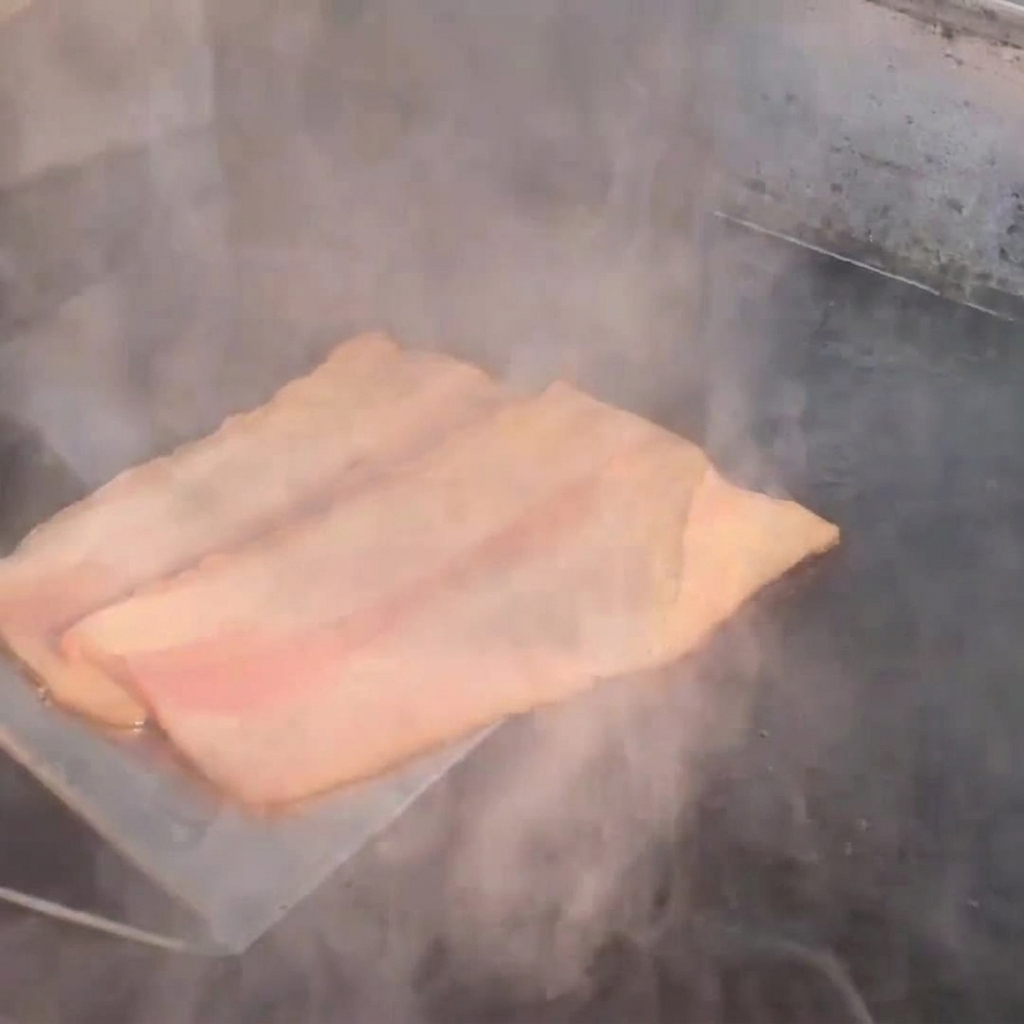 熱いフライパンの上で湯気を立てながら焼かれているベーコンのストリップ。