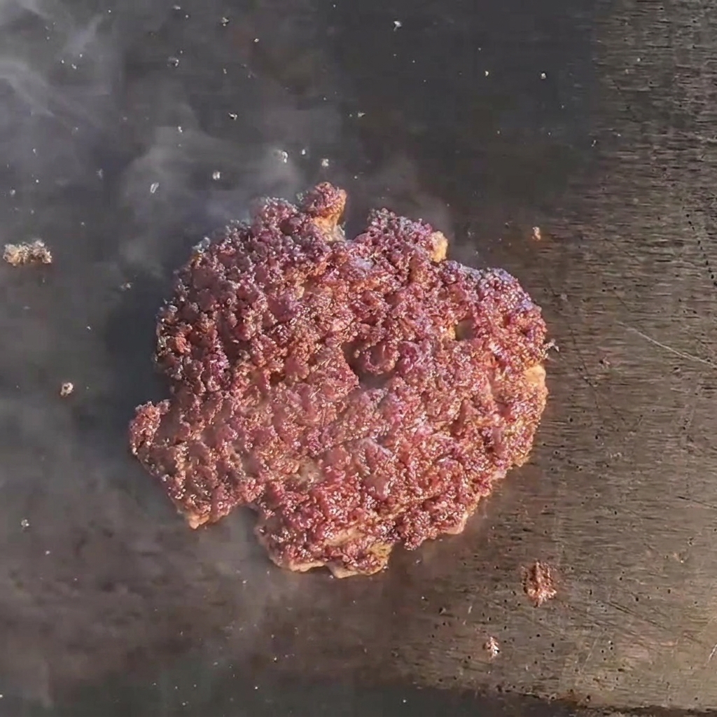 フライパンの上で、焼けたパティの上に溶けかかっているチーズ。