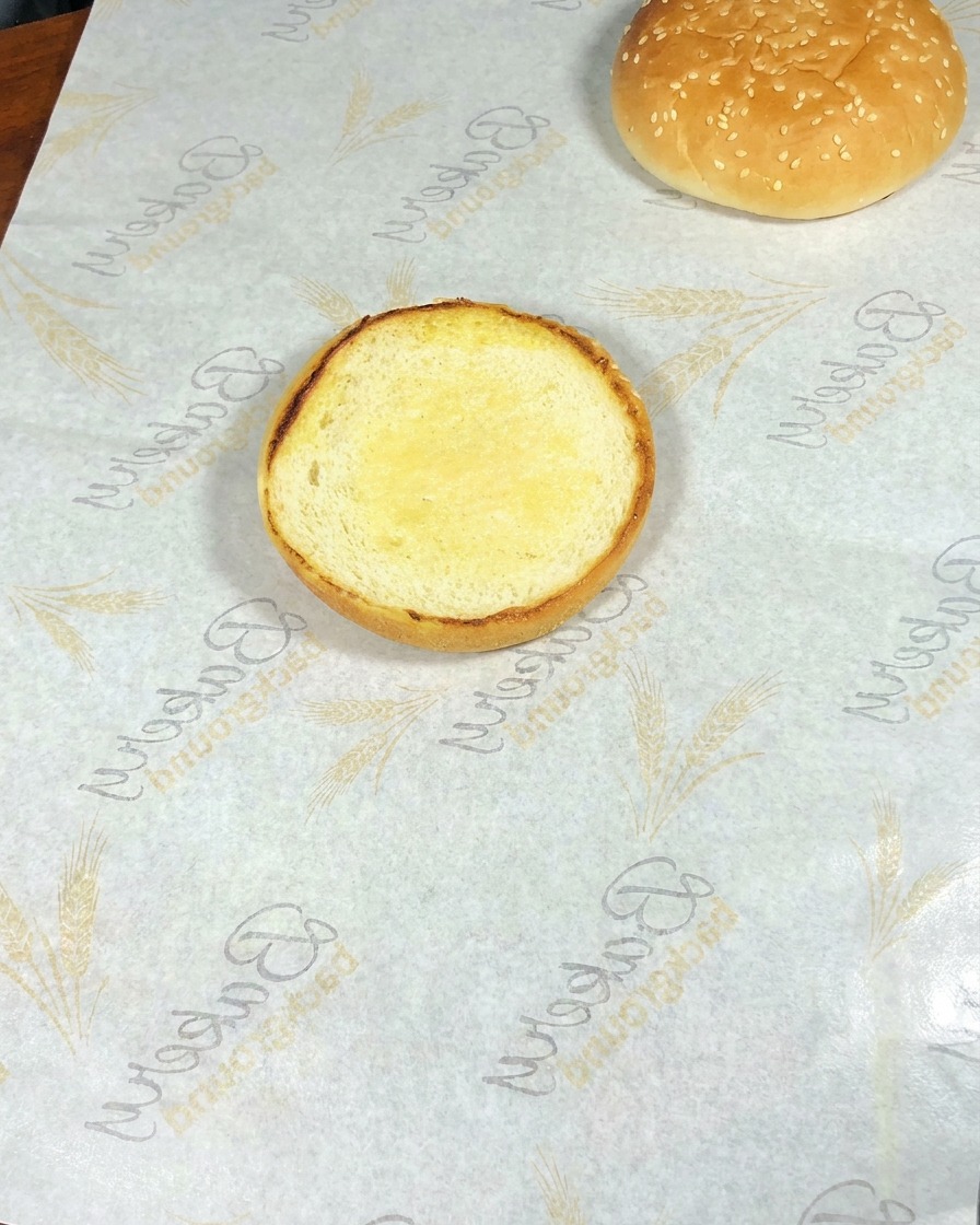 バンズにレタス、チーズ卵、焼き海老、アボカドを順に重ねたバーガーのアップ。