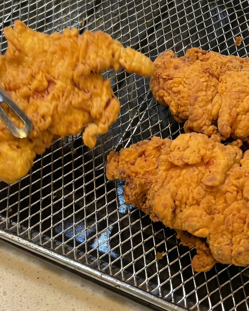 トングで揚げたてのチキンを持ち上げている様子。