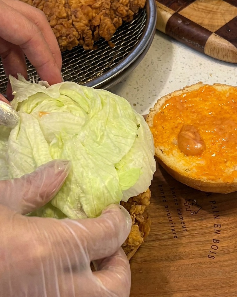 バンズにソース、チキン、レタスを挟んでいる様子。