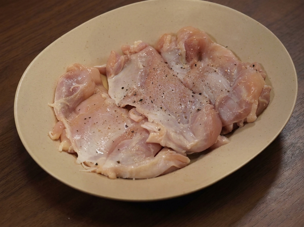 皿の上に並べられた、スパイスをまぶした生の鶏モモ肉。