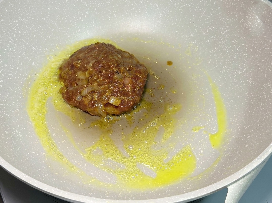弱火のフライパンでパティをじっくり焼く様子。