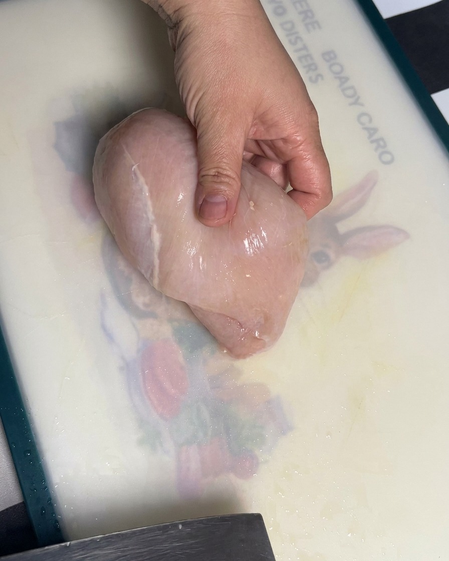 まな板の上で鶏むね肉を均一な厚さにスライスしている様子。