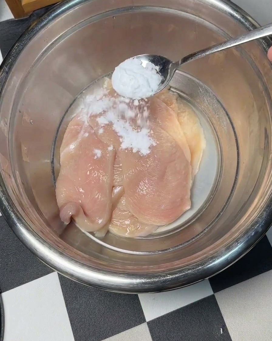 ボウルに入った鶏肉に重曹を振りかけている様子。