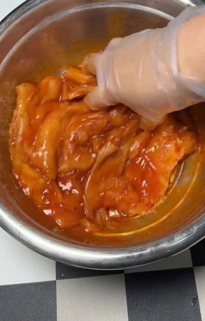 手袋をした手で、鶏肉と調味料をボウルの中でしっかり混ぜ合わせている様子。