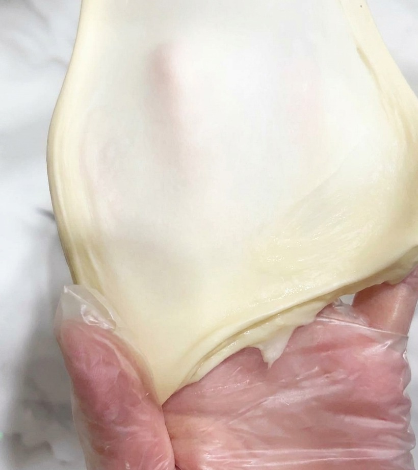 手で引き伸ばされた弾力のある生地が、光を通すほど薄い膜状になっている様子。