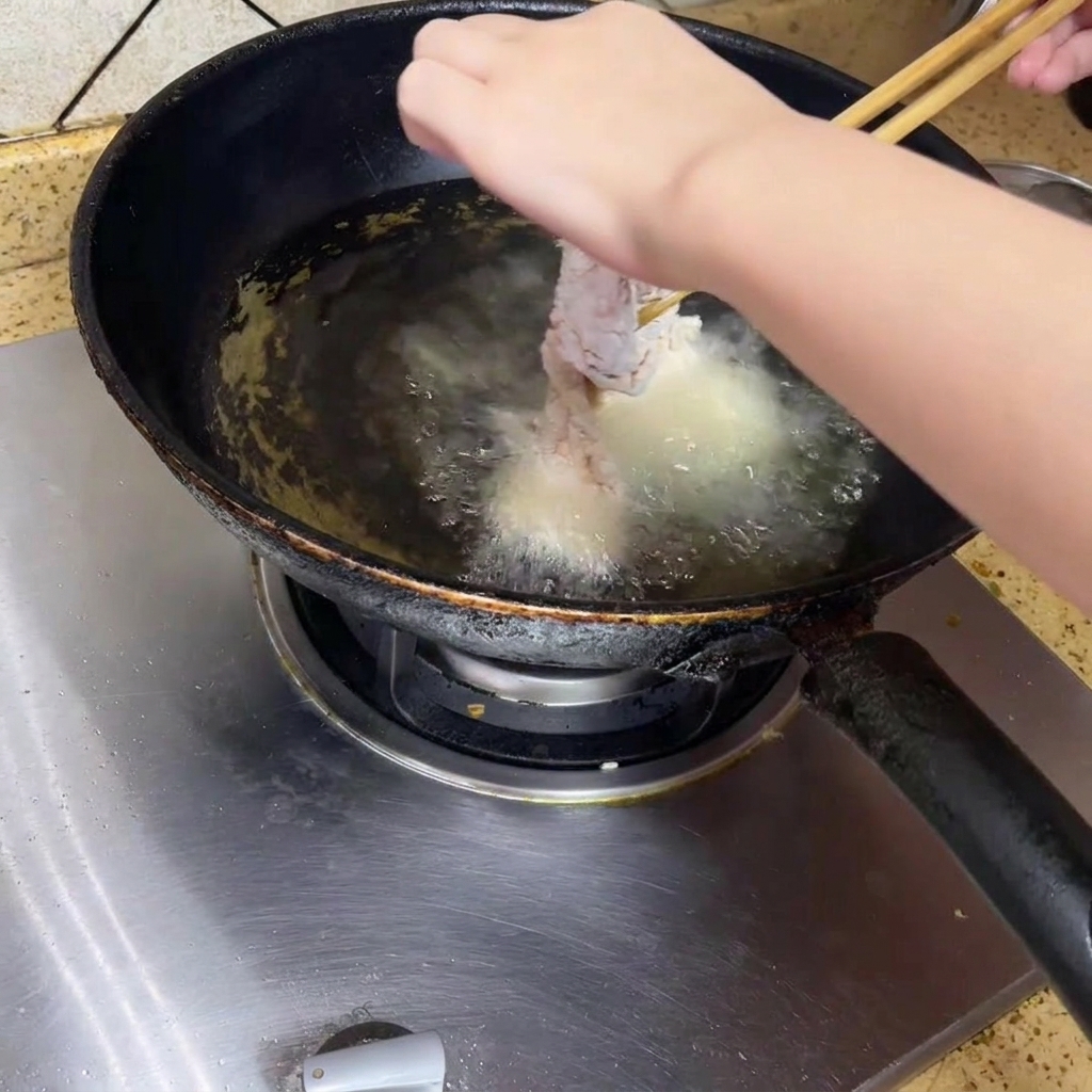 箸を使って、熱した油の中にパン粉をまぶした鶏肉をゆっくり入れている様子。