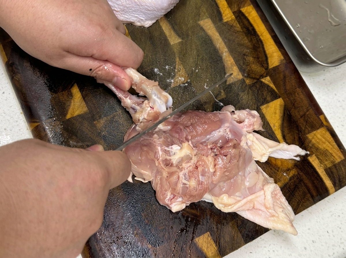 まな板の上で生の鶏もも肉を骨抜きしている手元のクローズアップ。