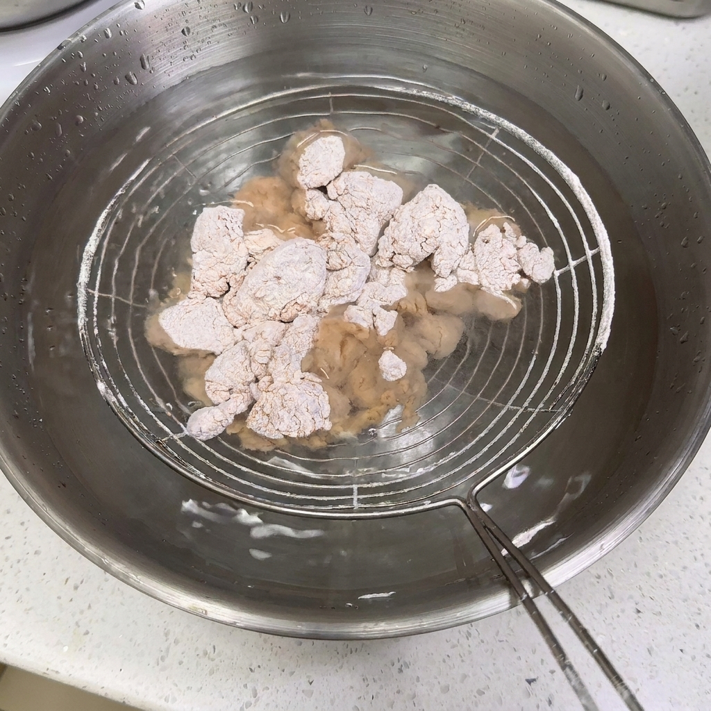 粉をまぶしたチキンを、金網に乗せて水を入れたボウルに沈めている様子。